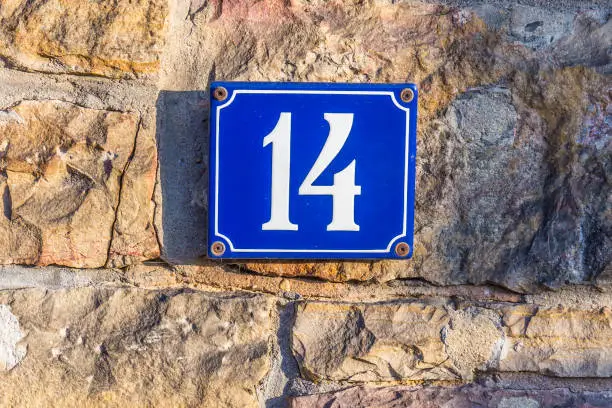 house number fourteen made of enamel at an old stone house wall