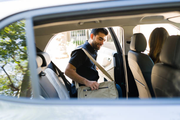 Happy driver picking up a new passenger Handsome male passenger smiling and getting on a rideshare car while talking to the female driver riding stock pictures, royalty-free photos & images