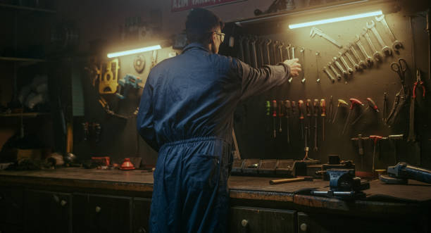 istock Young blacksmith male person picking up his tools from the bench to do work 1354259614