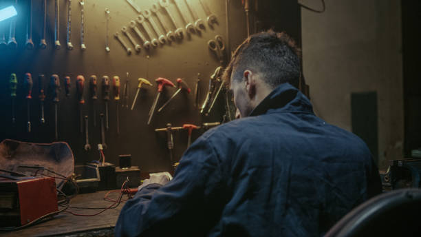 istock Young workshop owner man with workwear, sitting on chair and solder on workbench 1354260456