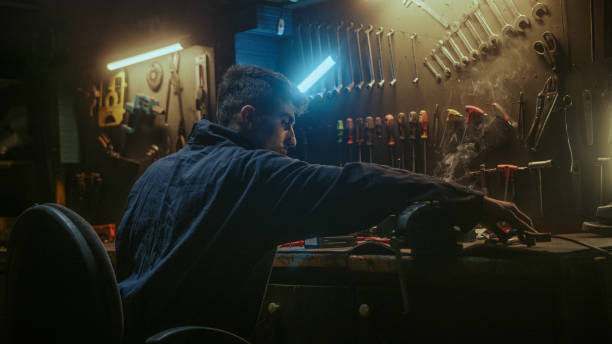 istock Young blacksmith man with workwear, taking solder tool, sitting on chair and do solder. 1354260515