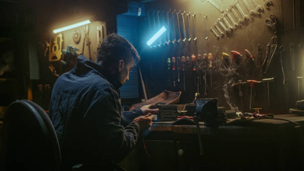 istock Young blacksmith man with workwear, taking solder tool, sitting on chair and do solder. 1354260709