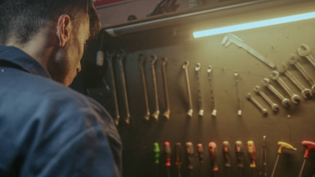 istock Young blacksmith male person picking up his tools from the bench to do work 1354260950