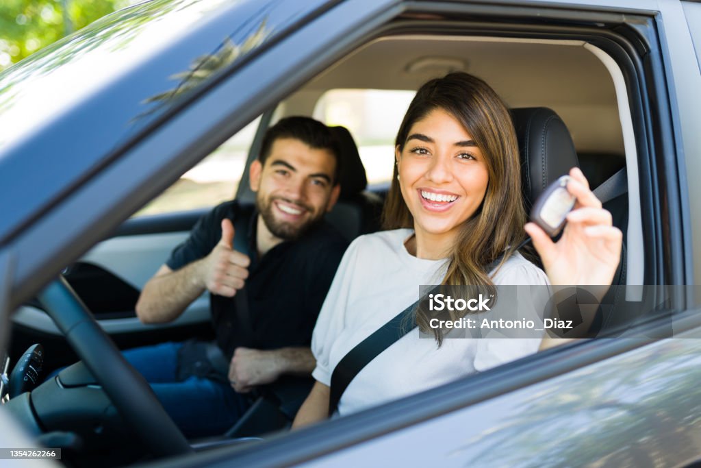 Latin couple taking their new car for a ride Gorgeous woman showing her keys after buying a new car. Excited couple giving a thumbs up to their rental car Car Stock Photo