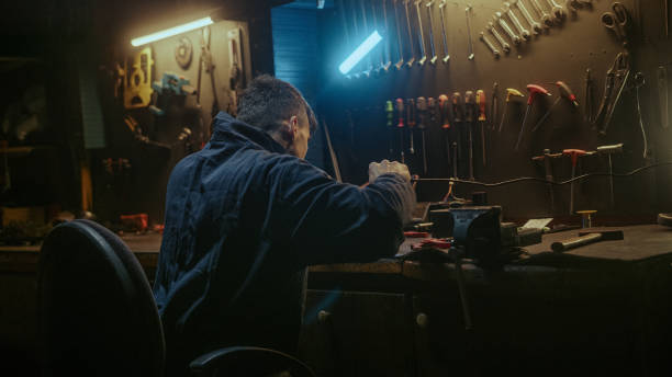 istock Young blacksmith man with workwear, taking solder tool, sitting on chair and do solder. 1354262705