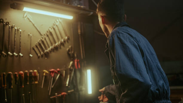 Determined young blacksmith in blue overalls checking his tools and supplies to get to work in his workshop