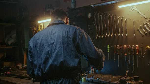 istock Young determined blacksmith in blue overalls tightens screw with screwdriver and puts his tool in place 1354263301