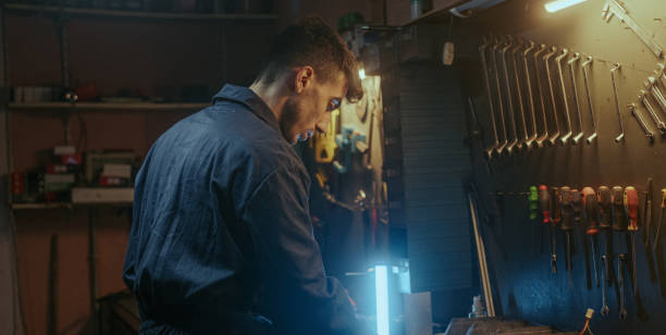 istock Young determined blacksmith in blue overalls tightens screw with screwdriver and puts his tool in place 1354263867