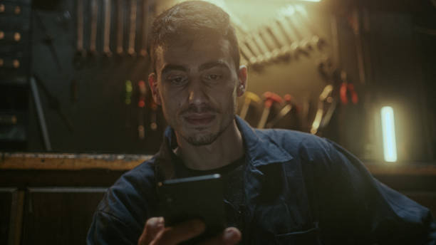 istock Young handsome blacksmith man sitting in front of the workbench, resting and using smartphone 1354263993