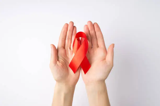 Photo of First person top view photo of young woman's hands holding red silk ribbon in palms symbol of aids awareness on isolated white background