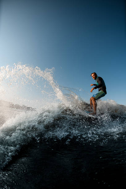 man skilfully riding wave on the wakesurf on the background of blue sky stock photo