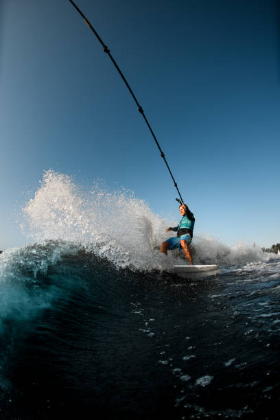 hombre montado en el wakesurf sosteniendo una cuerda de lancha a motor sobre el fondo del cielo azul - wakeboarding motorboating extreme sports waterskiing fotografías e imágenes de stock