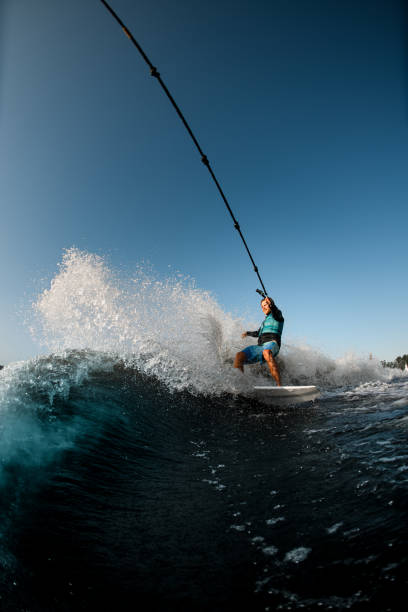 homem montando no wakesurf segurando corda de lancha no fundo do céu azul - wakeboarding motorboating extreme sports waterskiing - fotografias e filmes do acervo