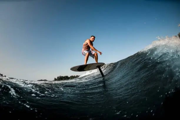 adult healthy sportive man skillfully riding on the wave with hydrofoil foilboard on background of blue sky