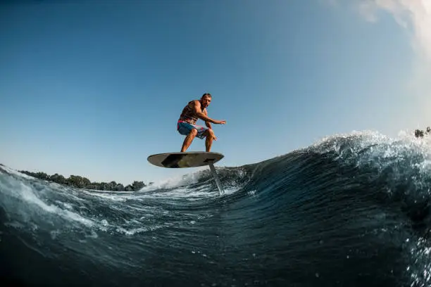 healthy athletic man balancing on the wave with hydrofoil foilboard on background of blue sky. Surfing, entertainment, leisure, water sports