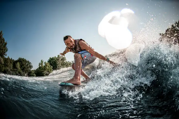 Close-up of adult athletic man riding down on splashing river wave on foilboard and having fun