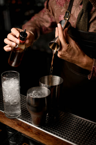 istock hand of bartender holds bottle with dispenser and other hand pours drink from jigger into shaker glass 1354273625