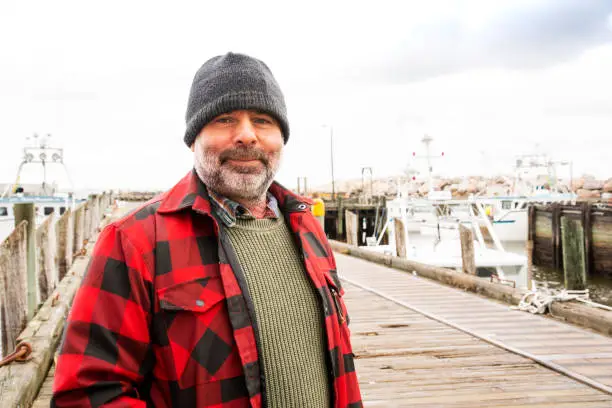 A mature commercial fisherman on a wharf with fishing  oats in the background