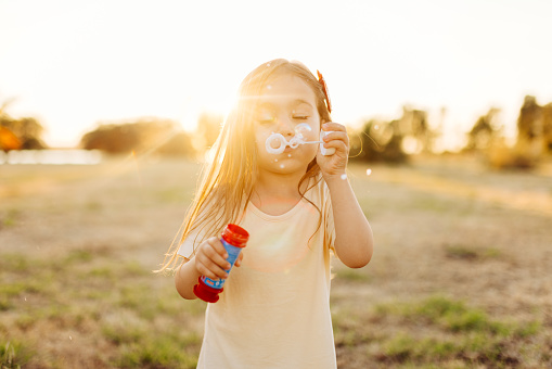 Children girl blowing soap bubbles outdoor. Little girl blowing soap bubbles in summer park.