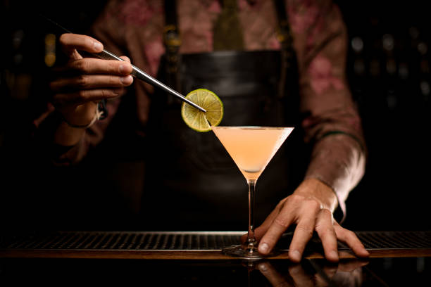 verre martini avec cocktail sur bar et main de barman décore le verre avec une tranche de citron - smooth part of colors yellow photos et images de collection