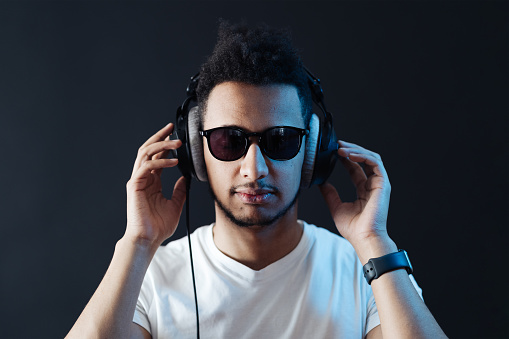 Cool handsome mid adult man listening music over headphones and looking away while dancing against white background