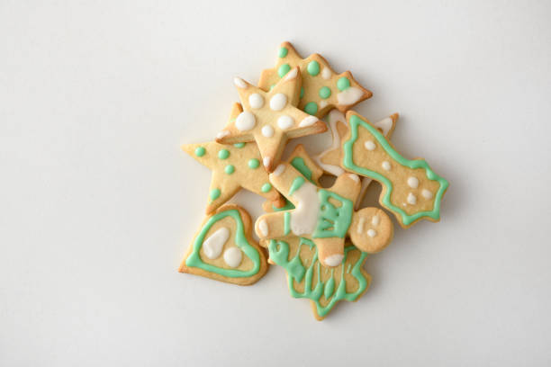 Assortment of Christmas shaped cookies decorated with white and green icing in a pile on white table. Top view. Horizontal composition.
