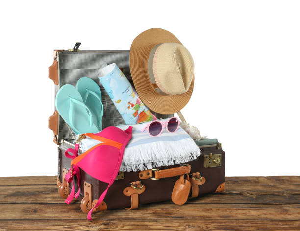 istock Open vintage suitcase with different beach objects packed for summer vacation on wooden table against white background 1354303394