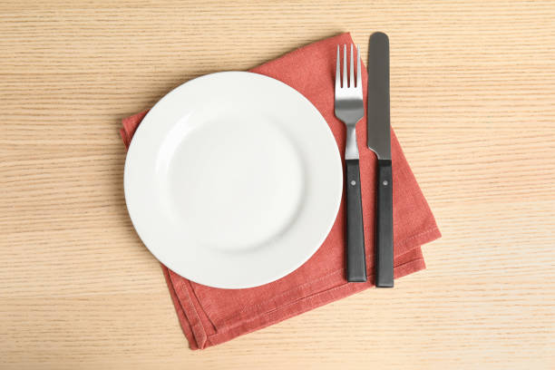 istock Empty white ceramic plate, towel and cutlery on wooden table, flat lay 1354304392