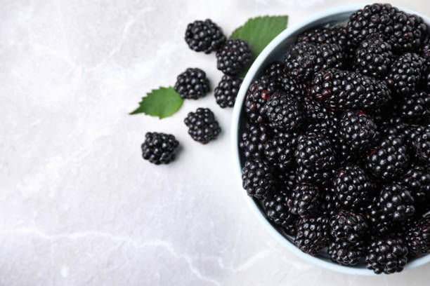 istock Fresh ripe blackberries in bowl on marble table, flat lay. Space for text 1354304489
