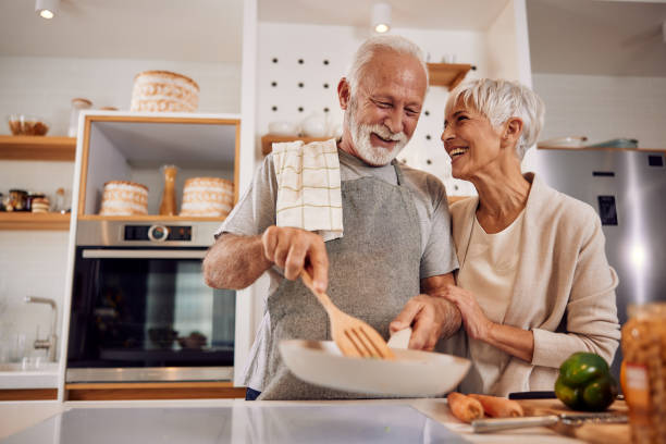 An older couple cooking a healthy vegan meal with vegetables together stock photo
