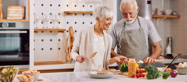 des aînés heureux et en bonne santé préparent des aliments végétaliens à la maison - cooking senior adult healthy lifestyle couple photos et images de collection