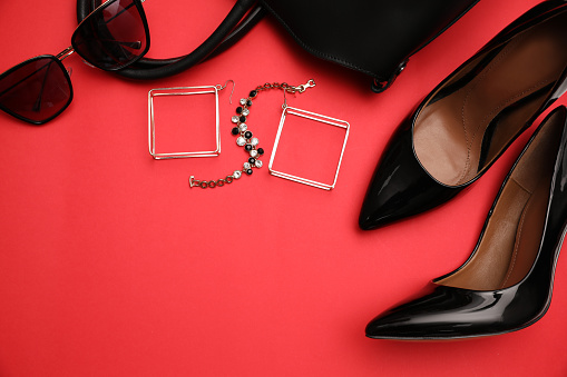 High heel shoes, bag and accessories on red background, flat lay. Space for text