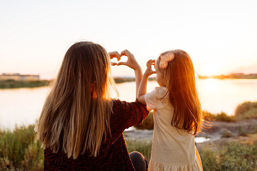 The concept of love, parenthood and a happy family. Mother and child daughter show heart from hands at sunset at nature