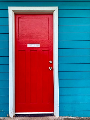 Vertical closeup photo of a vibrant red door on the front wall of a turquoise painted wooden plank house. Uralla, New England high country, NSW