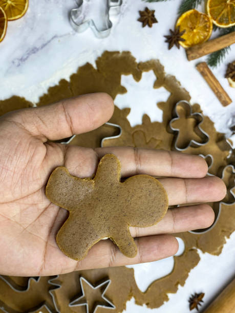 imagen de una persona irreconocible sosteniendo a un hombre de pan de jengibre sobre masa casera de galletas de pan de jengibre desplegada sobre fondo de efecto mármol, cortadores de galletas de metal, estrella, reno, copo de nieve, hoja de acebo, campana - candy cane christmas cookie raw food fotografías e imágenes de stock