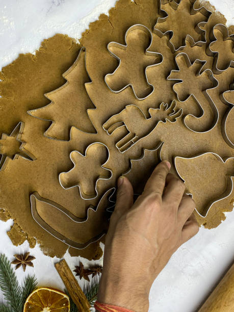 imagen de masa de galleta casera de pan de jengibre desplegada sobre fondo de efecto mármol, persona irreconocible usando cortadores de galletas de metal, árbol de navidad, estrella, reno, caña de caramelo, copo de nieve, hoja de acebo, campana y pan de - candy cane christmas cookie raw food fotografías e imágenes de stock