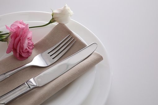 Elegant cutlery with napkin and flowers on white table, closeup