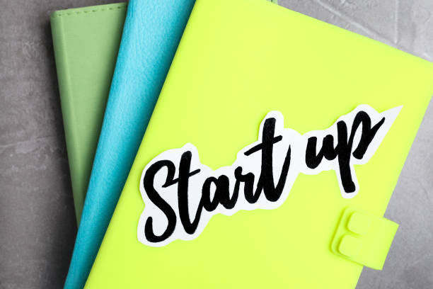 istock Sheet of paper with phrase Start Up and notebooks on grey table, top view 1354311946