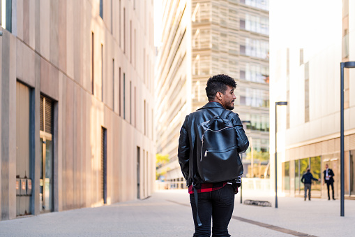 rear view of a stylish young latin man with a backpack walking in the city, concept of urban lifestyle