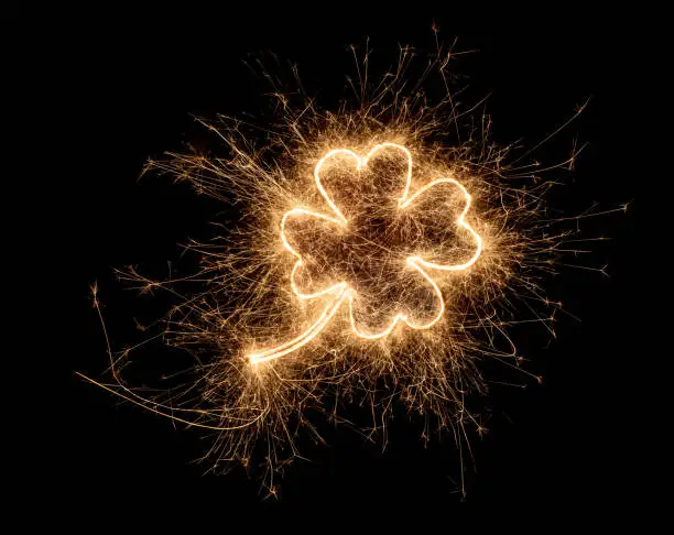 Photo of golden bright sparkler four leaf clover luck symbol  isolated on dark black background. silvester new year birthday celebration design pattern