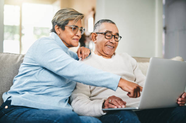 photo d’un couple de personnes âgées utilisant un ordinateur portable à la maison - laptop sofa men computer photos et images de collection