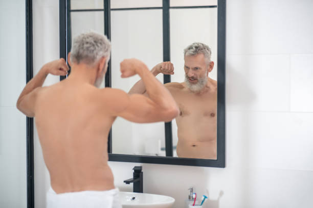 istock Man straining muscles of arms looking in mirror 1354348944