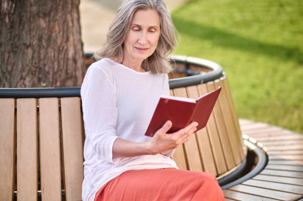 istock Woman reading book sitting on bench in park 1354351636
