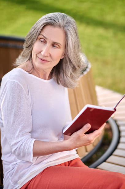 istock Meditative woman with book sitting on bench 1354351640