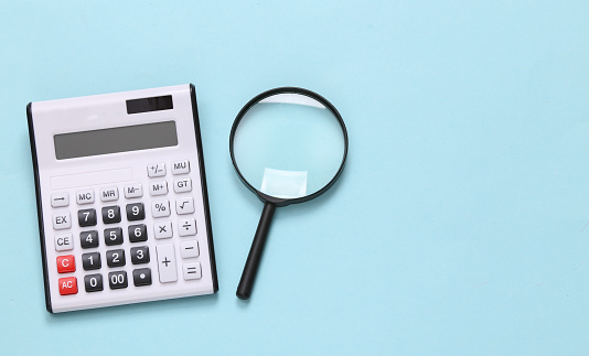 Calculator and magnifier on blue background. Top view. Copy space