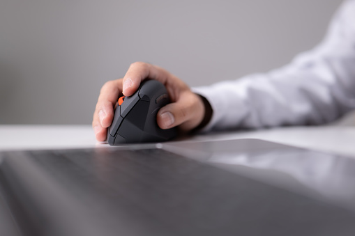A modern laptop and a vertical mouse in a panoramic shot. An ergonomic vertical mouse is used by a man in a shirt to prevent carpal tunnel syndrome. Designers, gamer, and medical suggestions.