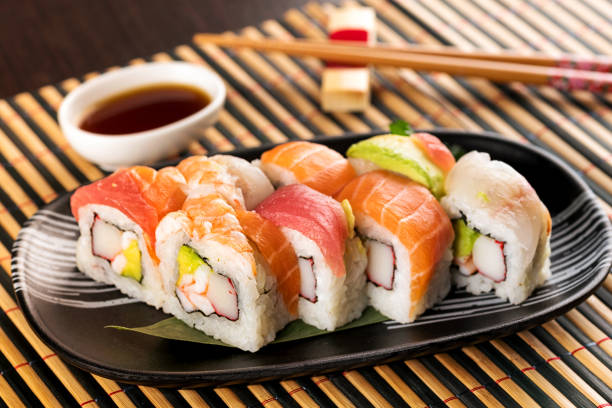 Set of rainbow uramaki sushi rolls with avocado Set of rainbow uramaki sushi rolls with tuna, salmon and avocado, served in restaurant on bamboo mat japanese cuisine food rolled up japanese culture stock pictures, royalty-free photos & images