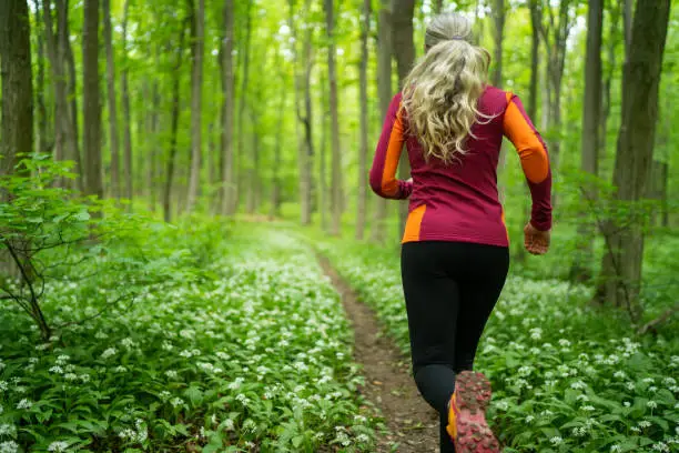 Back view of woman running in lush green vegetation through forest closer view