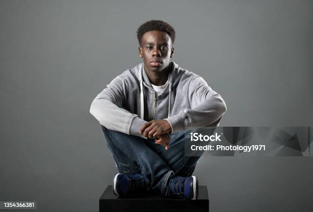 Young Black Man Posing Crosslegged In A Studio Stock Photo - Download Image Now - Teenager, African Ethnicity, African-American Ethnicity