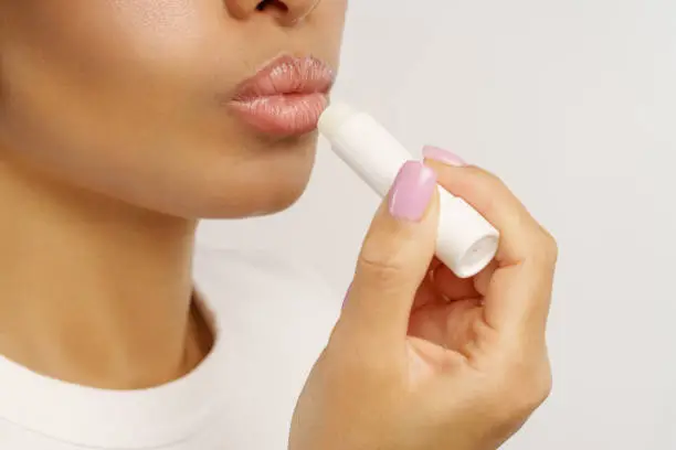 Photo of African woman apply hygienic balsam lipstick for lips moisturizing and protection from cold and wind